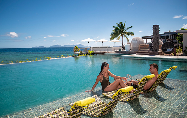 Couple relaxing by a luxury pool with a beautiful view of the ocean at VOMO, Fiji. 